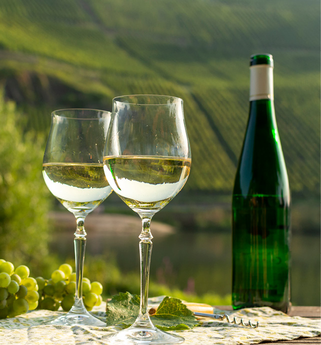 Two glasses and a bottle of Riesling White wine on a table, overlooking the views of a vineyard.