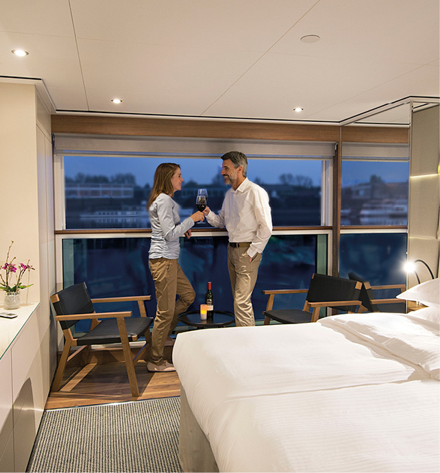 Couple enjoying night-time views from their balconied accommodation, with large bed and flat-screen TV