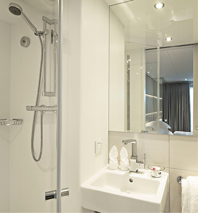 Pristine white-tiled bathroom, with shower, sink, large mirror, and two towels