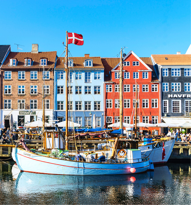 Visitors enjoying restaurants and bars in Copenhagen, Denmark on the waterfront, with sailing boats