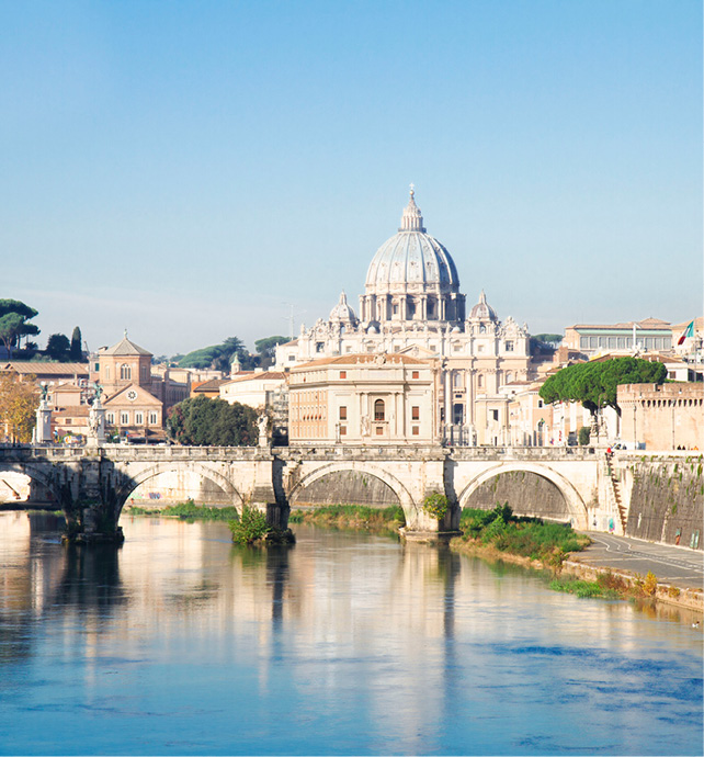 St. Peter’s Cathedral against the blue sky, seen from the River Tiber, with a bridge and surrounding architecture